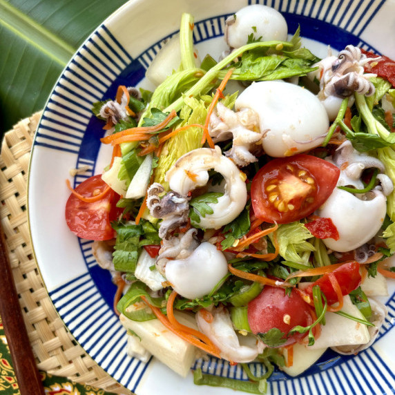 Top-view of yum pla muk with fresh vegetables in a white dish.