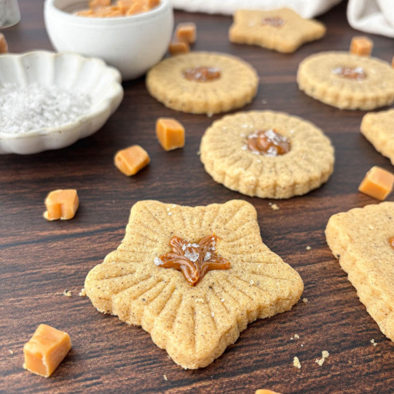Caramel Cookies on a wood table surrounded by bits of caramel.