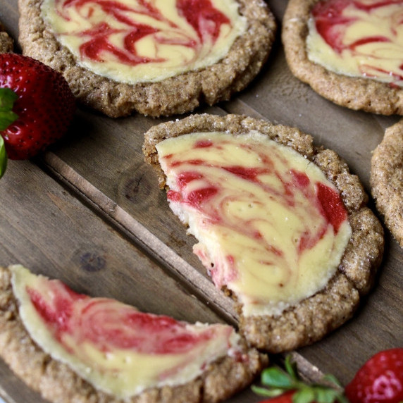 strawberry cheesecake cookies are arranged on a wooden board with fresh strawberries