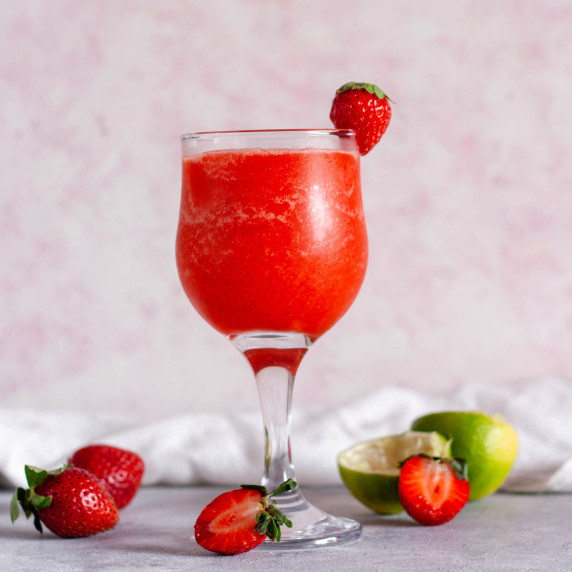 A strawberry daiquiri mocktail next to strawberries and limes.