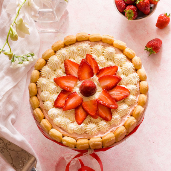strawberry charlotte cake on a pink surface with strawberries and flowers