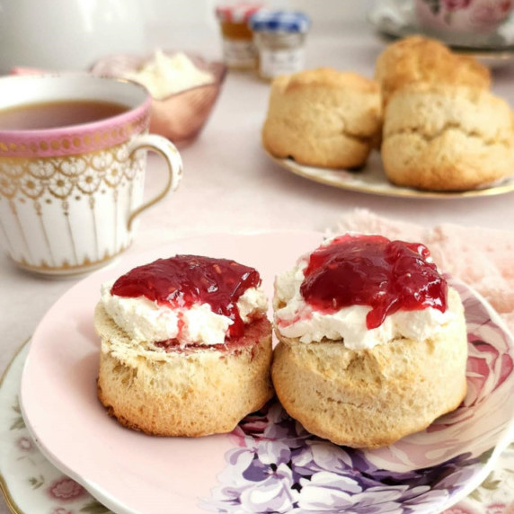 Close front angled shot of pink plate with 2 halves of British scones, with cream and raspberry jam