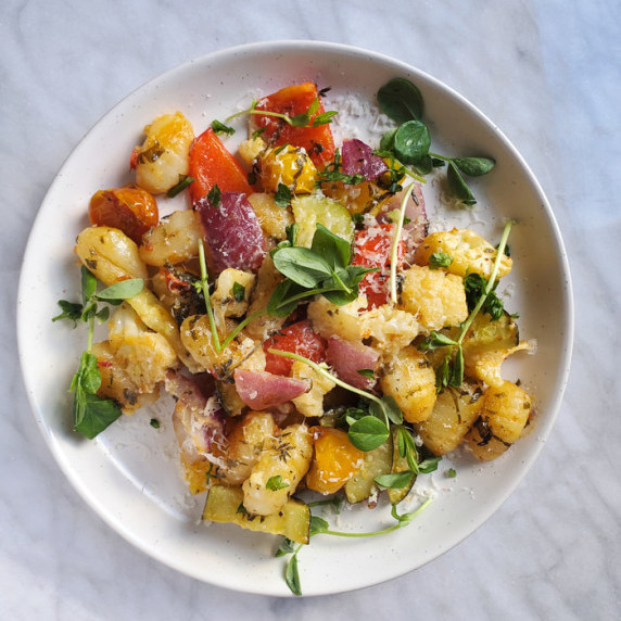 An assortment of roasted vegetables & gnocchi on a white plate against a marble background.