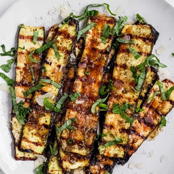 Grilled zucchini planks garnished with fresh basil ribbons and grated parmesan on a white plate.