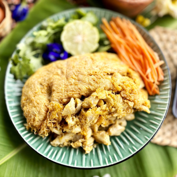 Thai crab omelette served on a green plate with fresh herbs, lime, and sliced carrots.