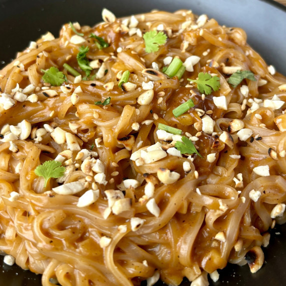 Close-up of Thai peanut noodles with crushed peanuts and fresh herbs garnish.