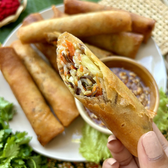 Hand presenting Thai vegetable spring roll, revealing the vegetable filling.