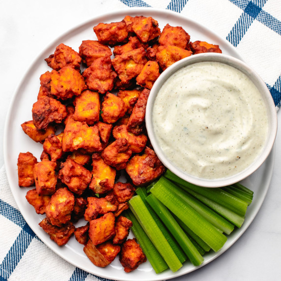 Baked buffalo tofu bites on a plate with celery sticks and a bowl of vegan ranch dressing.