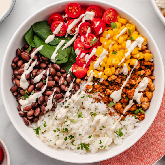 Tofu burrito bowl with black beans, corn, tofu meat, rice, cherry tomatoes, and spinach in a bowl.