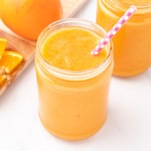 Orange carrot ginger smoothies in jars with a straw.