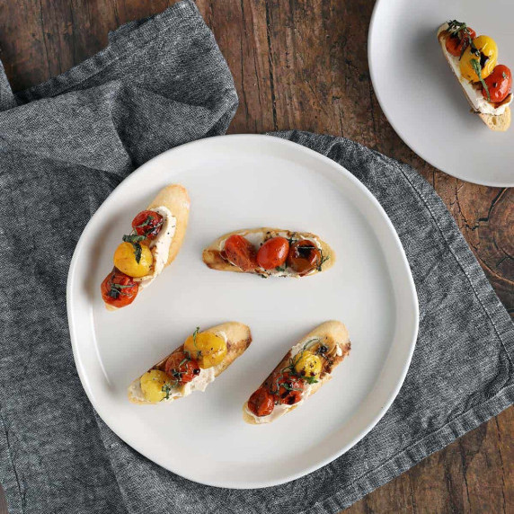 vegan goat cheese crostini with roasted tomatoes on a white plate