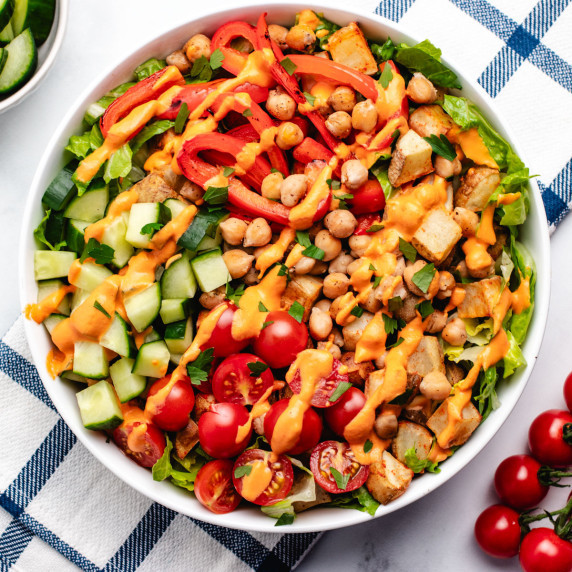 Roast potato and chickpea bowl with cucumber, cherry tomatoes, lettuce, and a red pepper dressing.