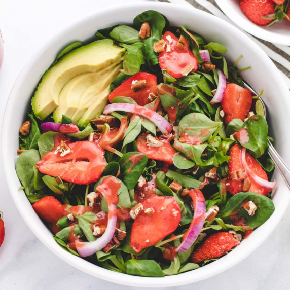 Strawberry spinach salad in a bowl with red onion and sliced avocado.