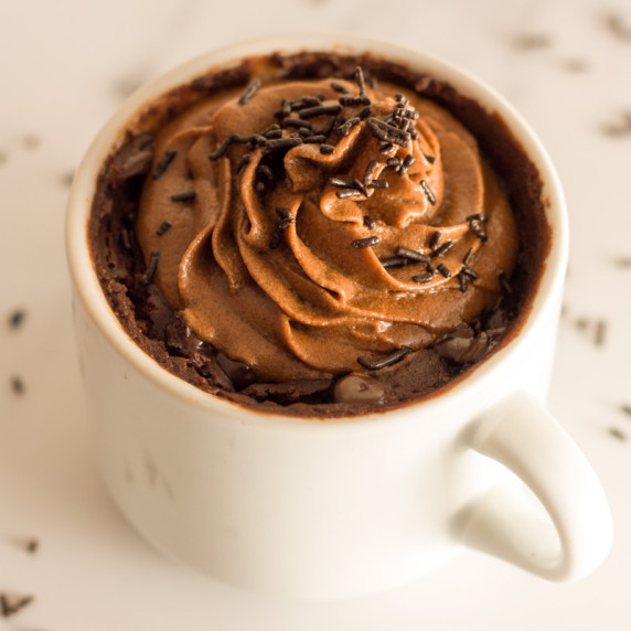 vegan mug brownie with chocolate frosting on top and chocolate sprinkles on a white surface