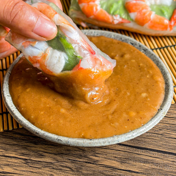 Close-up of fresh spring rolls dipped into peanut hoisin sauce.