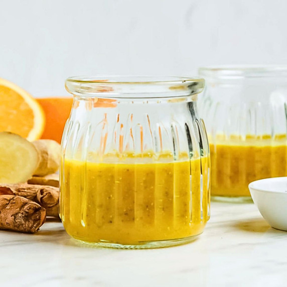 wellness shot in two glasses, some fresh ginger root and orange slices on the side