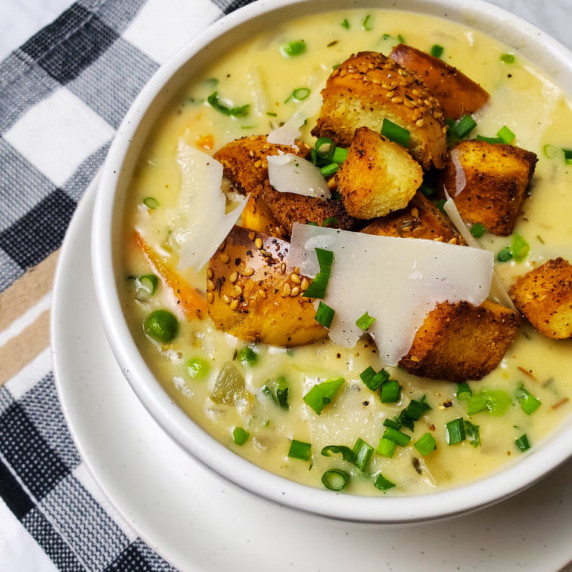Creamy chowder garnished with chives and shaved grana padano, served in a white bowl.
